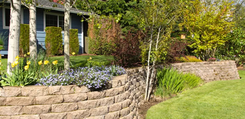 retaining wall with trees and flowers to support land above the slope of the yard