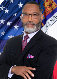 Barry L. Stanton standing in front of American flag and Prince George's County flag