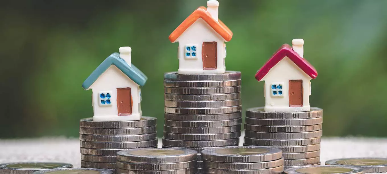 miniature houses sitting on stacks of coins