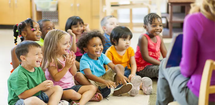 Daycare of 8 or more inspection, 9 children sitting around teacher, reading a book to the group