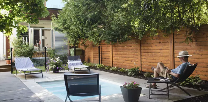 Fence residential backyard with posts facing in and drainage area under slats, pool, man reading