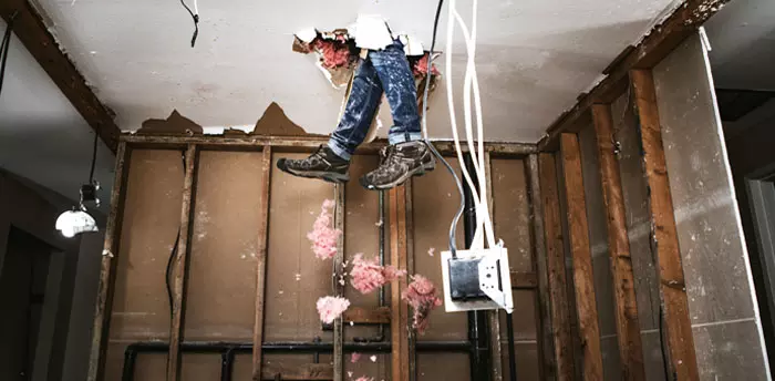 Unpermitted Construction, person's legs hanging thru broken ceiling with electrical box dangling and insulation falling